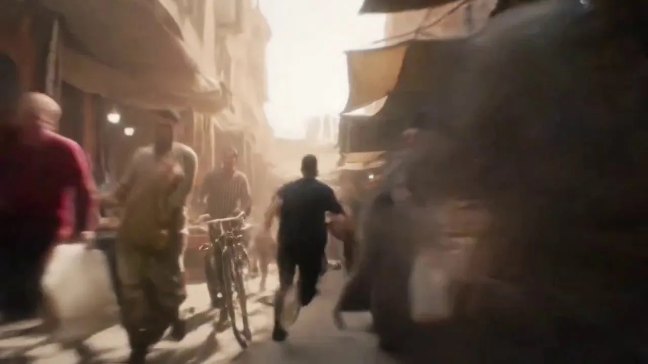 An intense FPV-style continuous shot weaves at full sprint through a bustling Moroccan street market